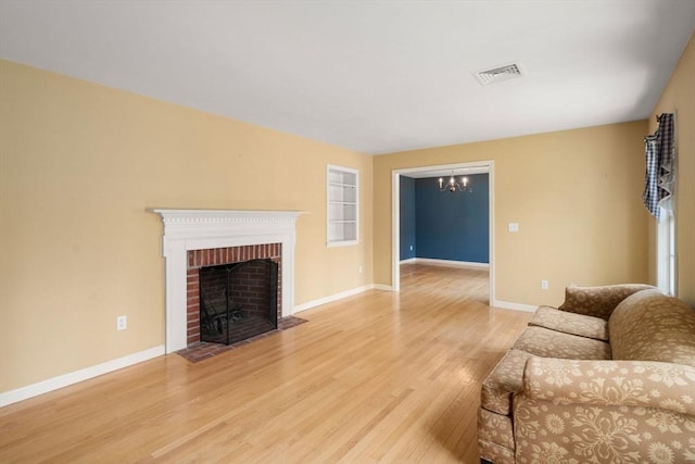 living room with visible vents, a brick fireplace, baseboards, a chandelier, and light wood-style flooring