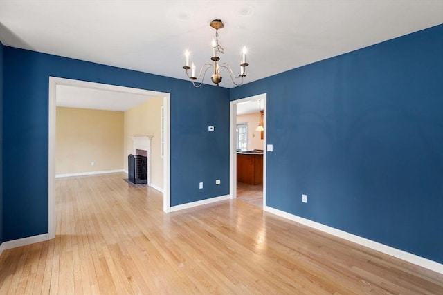 empty room featuring baseboards, a chandelier, a fireplace with flush hearth, and light wood finished floors