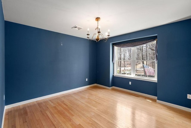 empty room with baseboards, light wood-type flooring, a chandelier, and visible vents