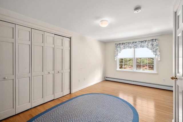 unfurnished bedroom featuring baseboards, a baseboard heating unit, light wood-style flooring, and a closet