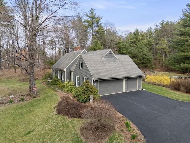 view of side of property with a shingled roof, a garage, a chimney, a lawn, and driveway