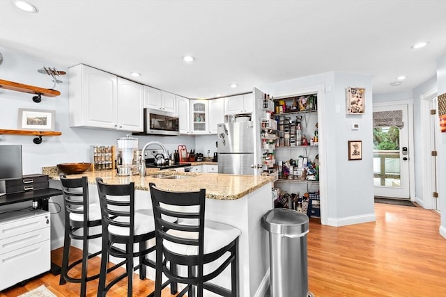 13 Emmet St Unit 1, Boston, MA 02127 - kitchen with stainless steel appliances, a peninsula, light stone countertops, white cabinets, and a breakfast bar