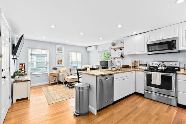 13 Emmet St Unit 1, Boston, MA 02127 - kitchen with stainless steel appliances, a wall mounted AC, light wood finished floors, a peninsula, and white cabinetry