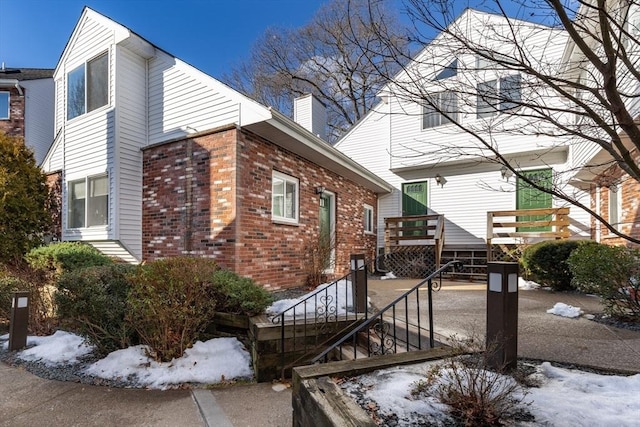 view of snow covered exterior featuring a chimney, brick siding, and a wooden deck