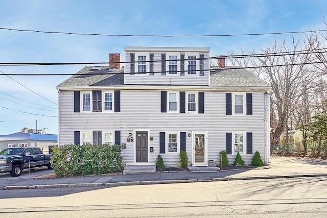 colonial-style house with a balcony, roof with shingles, and a chimney