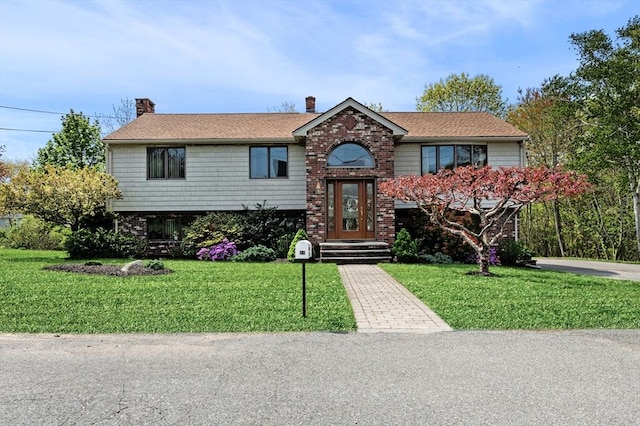 bi-level home featuring brick siding, a chimney, and a front lawn