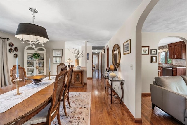 dining room with arched walkways, light wood finished floors, baseboards, and a chandelier