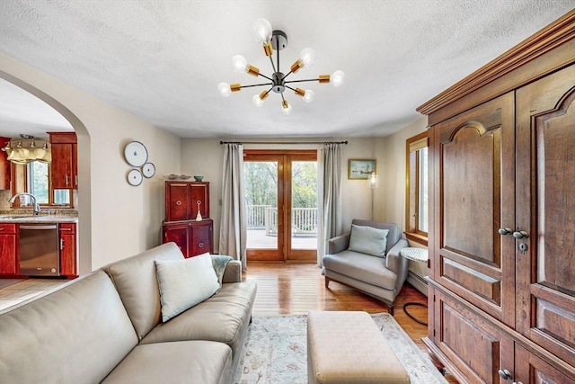 living room featuring arched walkways, a chandelier, light wood-style flooring, french doors, and a textured ceiling