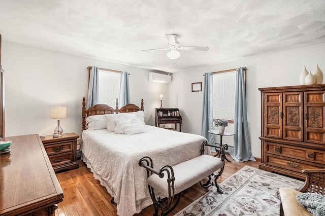 bedroom with an AC wall unit, light wood-style floors, and a ceiling fan