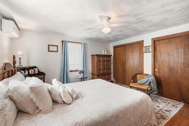 bedroom featuring a wall unit AC, multiple closets, wood finished floors, and ceiling fan