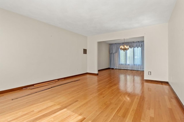 empty room with baseboards, light wood finished floors, and a chandelier
