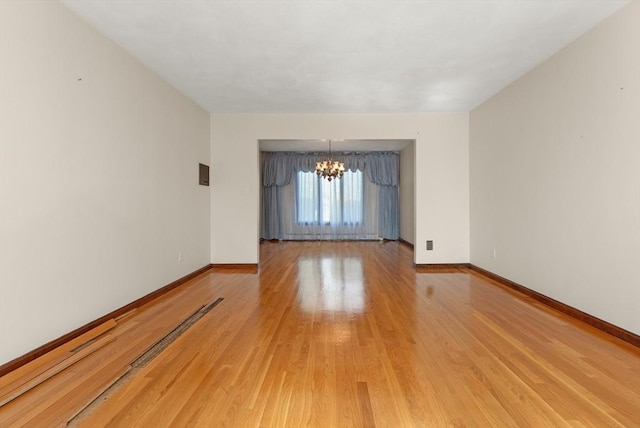 empty room with an inviting chandelier, light wood finished floors, and baseboards