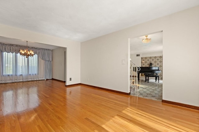 spare room with stairs, baseboards, a notable chandelier, and wood finished floors