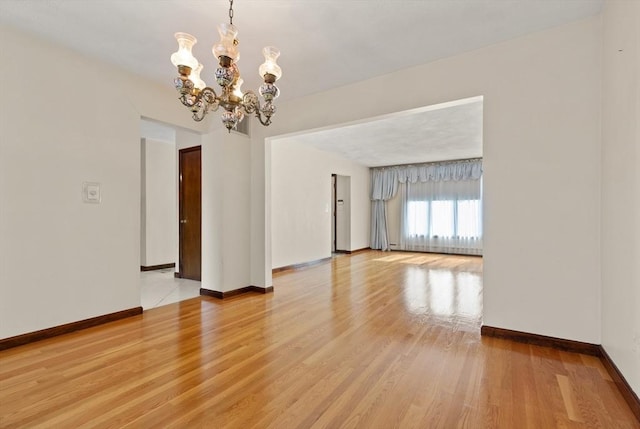 spare room featuring baseboards, a notable chandelier, and light wood-style floors