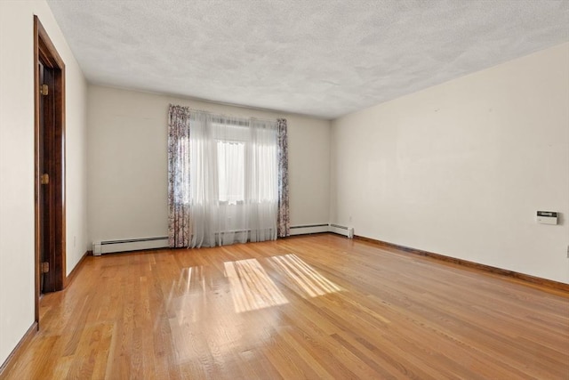 empty room with a textured ceiling, baseboards, baseboard heating, and light wood-type flooring
