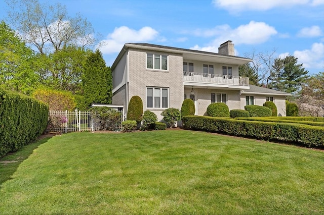 view of front facade featuring fence, a balcony, a front yard, a chimney, and brick siding