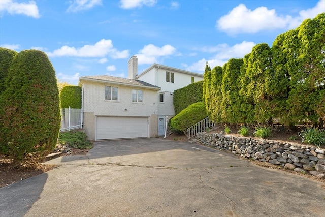 view of side of home with an attached garage, aphalt driveway, fence, and a chimney