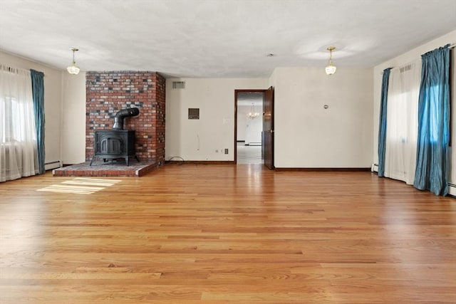 unfurnished living room with light wood-style floors, a wood stove, baseboards, and visible vents