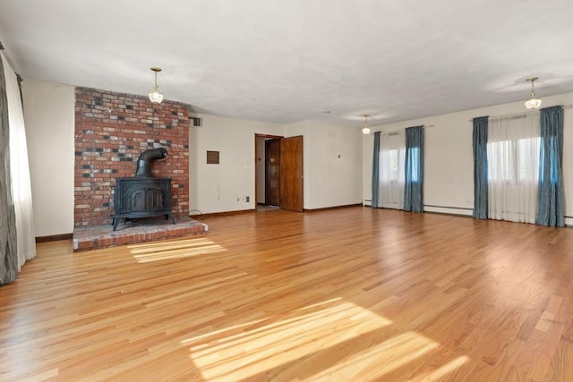 unfurnished living room with baseboards, a wood stove, light wood finished floors, and a baseboard radiator