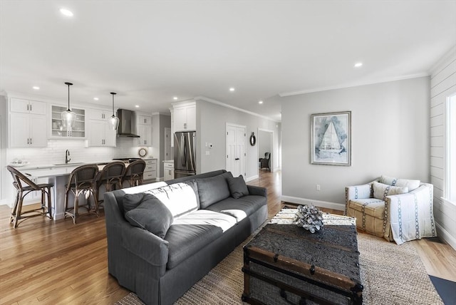 living room featuring ornamental molding, sink, and light hardwood / wood-style flooring