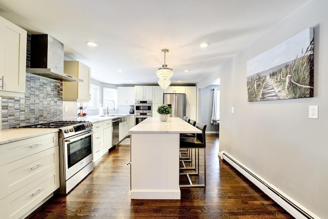 kitchen with pendant lighting, wall chimney range hood, stainless steel appliances, a kitchen island, and a baseboard radiator