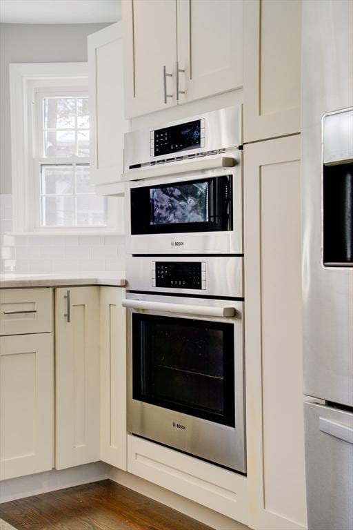 kitchen featuring tasteful backsplash, dark wood-type flooring, stainless steel double oven, and refrigerator with ice dispenser