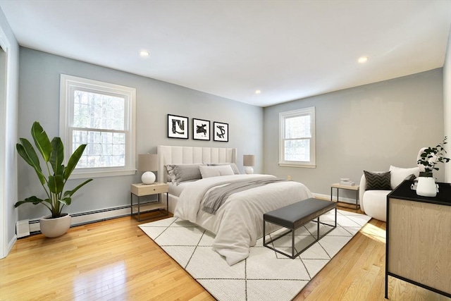 bedroom with multiple windows, light hardwood / wood-style flooring, and a baseboard heating unit