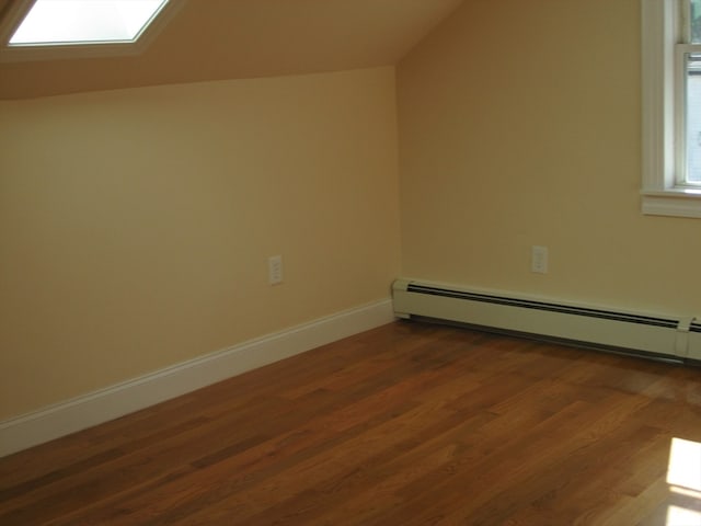 additional living space with vaulted ceiling with skylight, dark hardwood / wood-style flooring, and baseboard heating