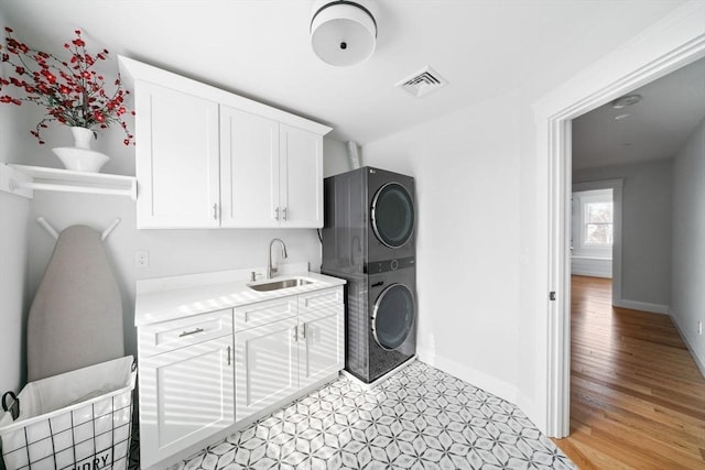 washroom featuring sink, cabinets, and stacked washer and clothes dryer