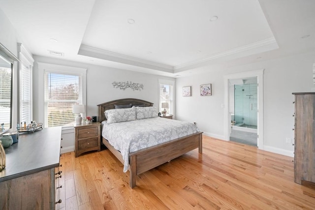 bedroom with crown molding, connected bathroom, light wood-type flooring, and a tray ceiling