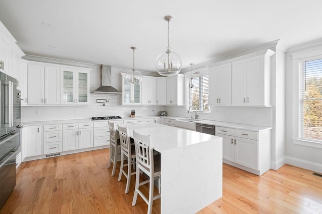 kitchen with wall chimney exhaust hood, sink, a kitchen breakfast bar, a kitchen island, and white cabinets