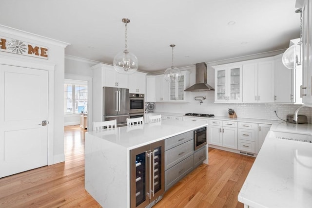 kitchen featuring wall chimney exhaust hood, white cabinetry, a center island, pendant lighting, and stainless steel appliances