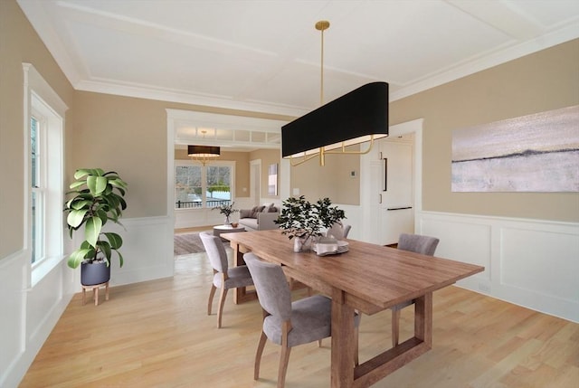 dining area with ornamental molding, a wainscoted wall, light wood finished floors, and a decorative wall