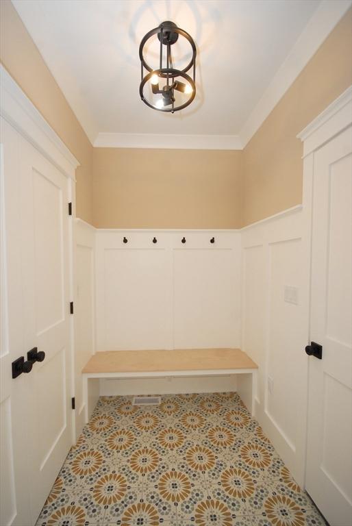 mudroom with tile patterned floors, wainscoting, and a decorative wall