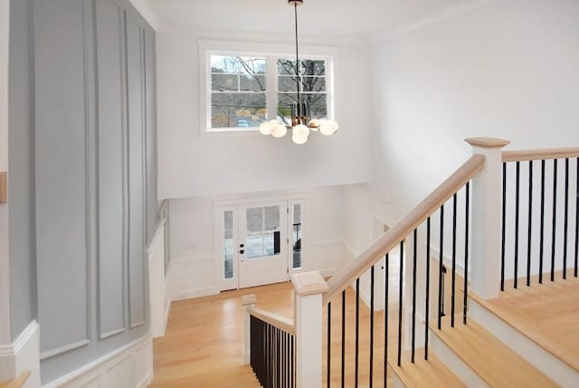 entryway with an inviting chandelier, ornamental molding, light wood finished floors, a decorative wall, and stairs