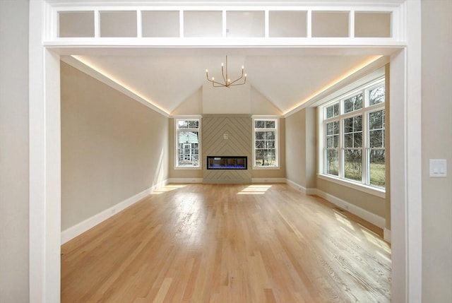 unfurnished living room featuring light wood-style flooring, a chandelier, vaulted ceiling, a glass covered fireplace, and baseboards
