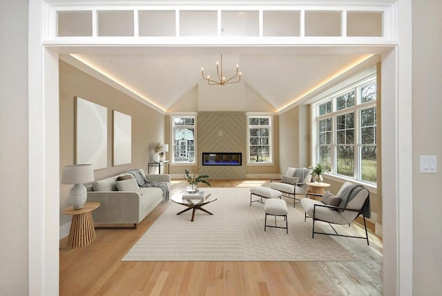 living room with an inviting chandelier, a glass covered fireplace, wood finished floors, and baseboards