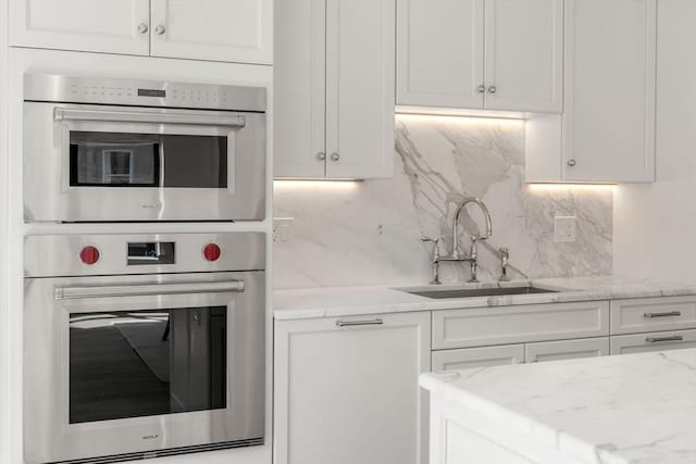 300 Boylston St Unit 907, Boston, MA 02116 - kitchen with double oven, white cabinetry, light stone counters, a sink, and backsplash
