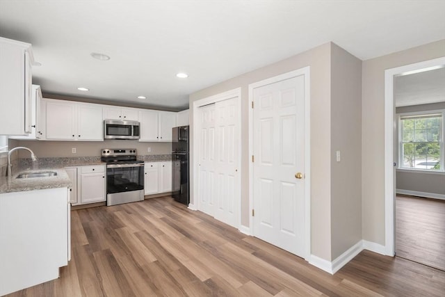 kitchen with sink, light stone counters, light wood-type flooring, stainless steel appliances, and white cabinets