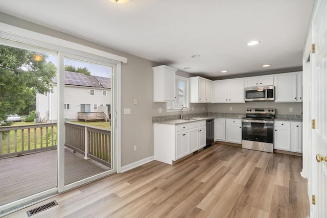 kitchen featuring sink, light hardwood / wood-style flooring, appliances with stainless steel finishes, light stone counters, and white cabinets