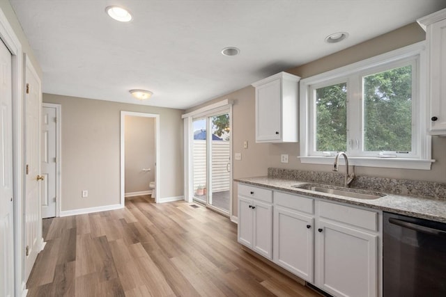 kitchen with sink, white cabinets, dishwashing machine, light stone counters, and light hardwood / wood-style flooring