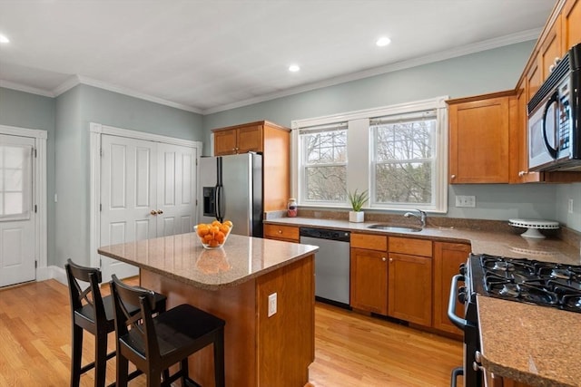 kitchen featuring a sink, a center island, black appliances, and light wood-type flooring