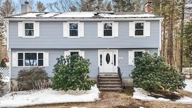 colonial house featuring entry steps, a chimney, and roof mounted solar panels