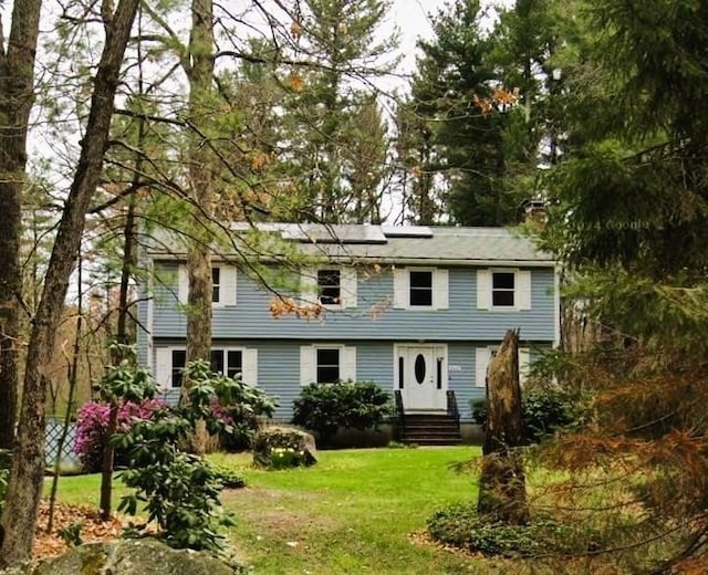 colonial house featuring entry steps, a front lawn, a chimney, and roof mounted solar panels