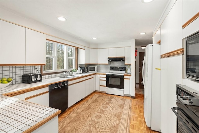 kitchen featuring tile countertops, under cabinet range hood, a sink, white cabinets, and black appliances