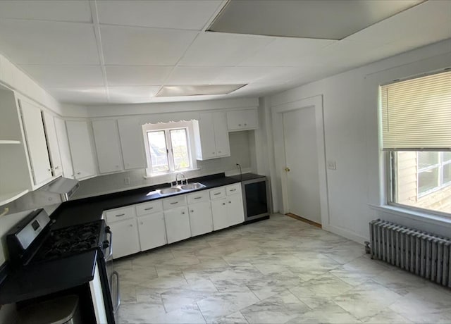 kitchen featuring dark countertops, a sink, stainless steel range with gas cooktop, radiator, and white cabinetry