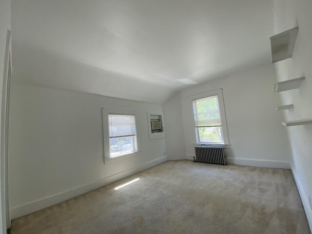 spare room with carpet floors, radiator, baseboards, and vaulted ceiling