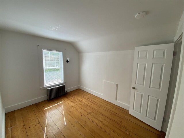 bonus room with light wood-style floors, radiator, baseboards, and lofted ceiling