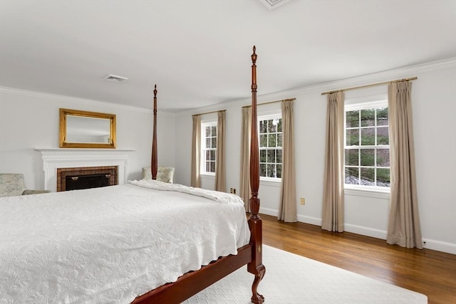 bedroom featuring crown molding, hardwood / wood-style floors, and a brick fireplace