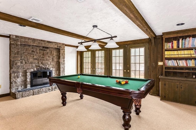 game room with light carpet, french doors, a textured ceiling, beamed ceiling, and a stone fireplace